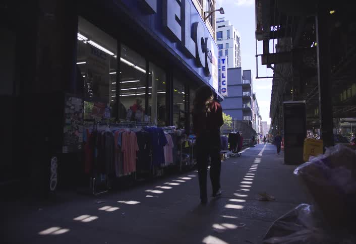 A person walks beside racks of clothes displayed outside a shop in the city under the shadow of an elevated structure