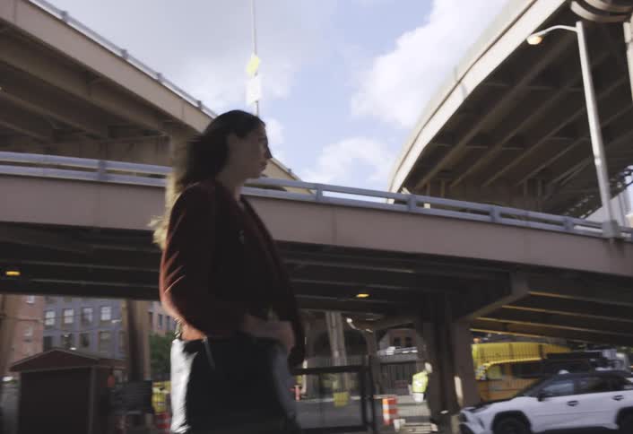 Female pedestrian walks past a gated parking area located under a network of overpasses in the city