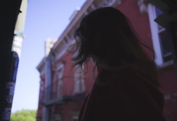 A woman walks up a staircase in an urban alleyway turning her head slightly as she ascends