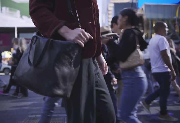 A closeup shot of a woman walking through a city street focusing on her hand and black handbag