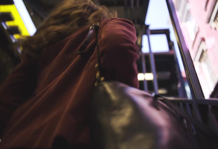 Woman wearing red coat and handbag rapidly ascends a set of stairs inside a structure