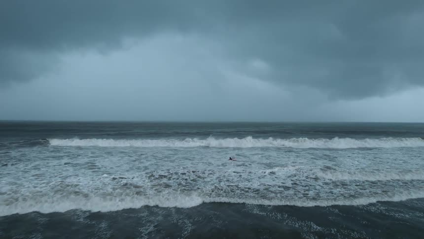 Person swims in rough weather and waves as dark clouds approach