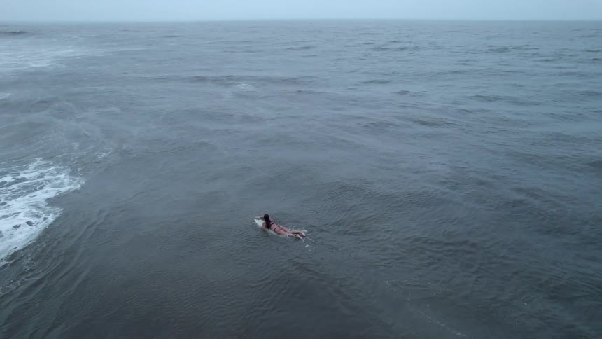 Woman paddles on surfboard near large waves and a land mass
