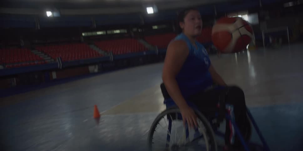 Two people in wheelchairs are playing basketball on an indoor court
