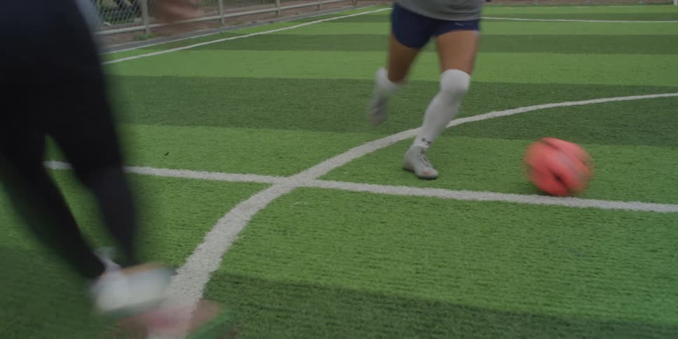 Two female soccer players in motion fighting for the ball on a synthetic grass field