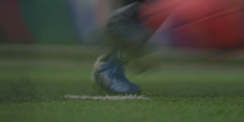 A soccer player strikes a red and black ball on a lush green field