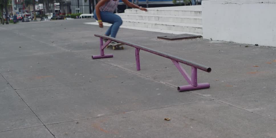 A skateboarder is grinding on a purple rail near white stairs and modern urban buildings