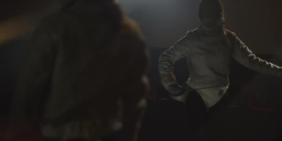 Two people in a dark room are wearing protective gear as they compete in fencing