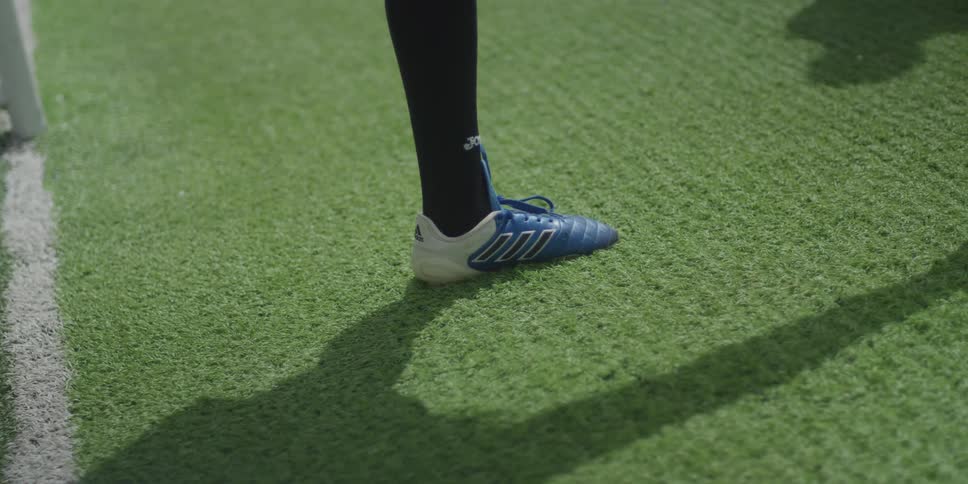 A person wearing cleats is on artificial turf warming up their legs