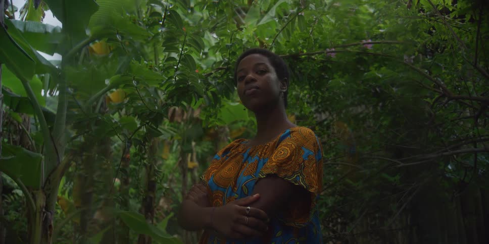 A woman is standing by the green trees