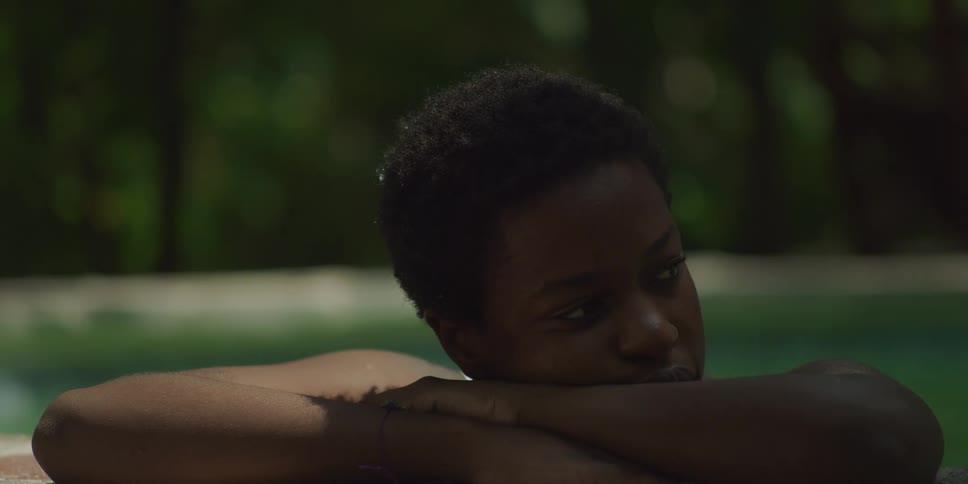 A black woman stands in a swimming pool and rests against the edge