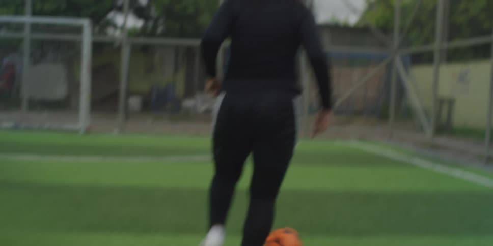 Three young female soccer players are training with a soccer ball as one dribbles it toward the goal with the other two following her on the field at midday