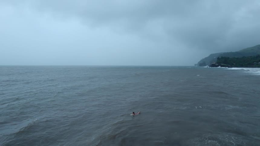 Aerial view of a woman on a surfboard isolated in the ocean on a cloudy day