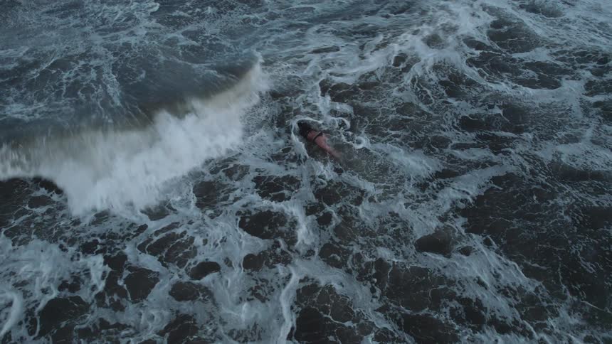 A lone surfer balances on a board gliding over turbulent ocean waves streaked with foamy crests