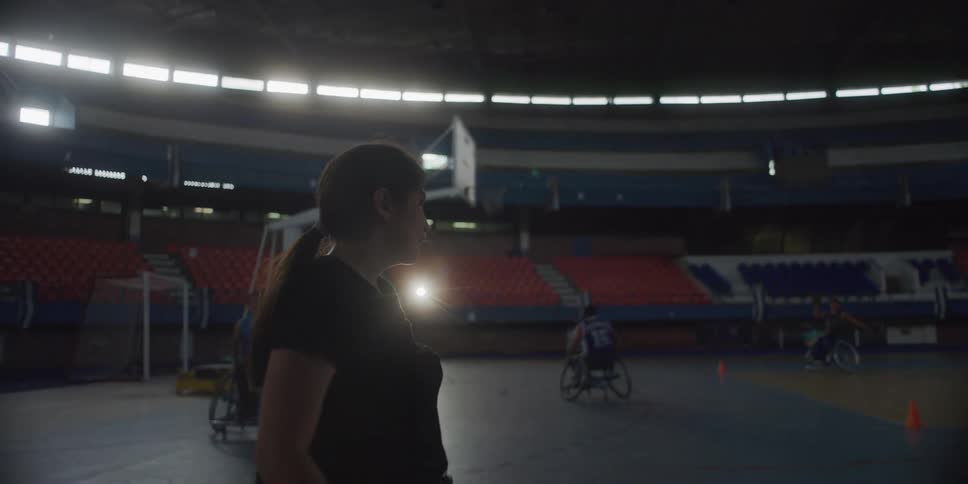 A woman watches a group of disabled people play basketball in a large arena
