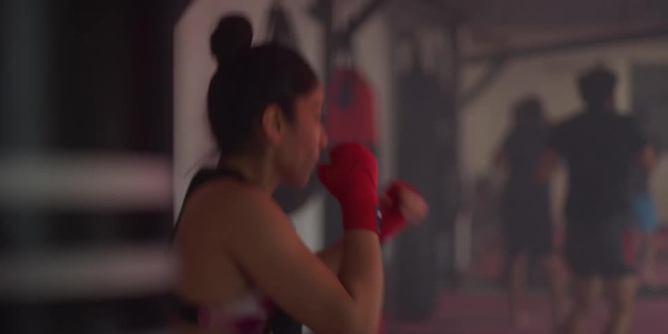 Woman with red training gloves in a fighting stance inside a boxing gym