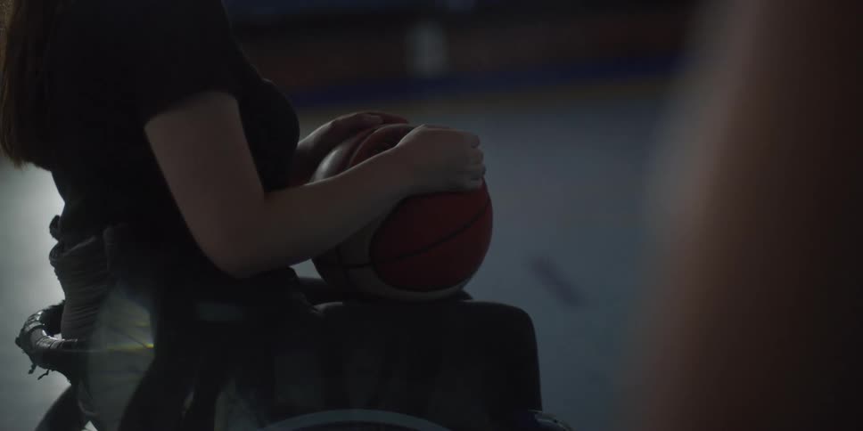 Woman is sitting in room holding a basketball while a finger blocks the right side of the camera