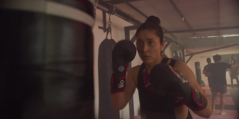 Woman wearing gloves with a focused expression punching and kicking a punching bag