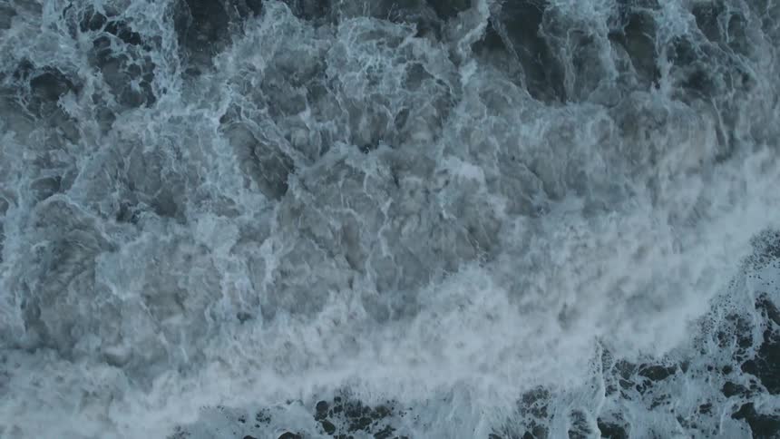The ocean waves hit the beach creating ripples and foam in the water under the midday sun