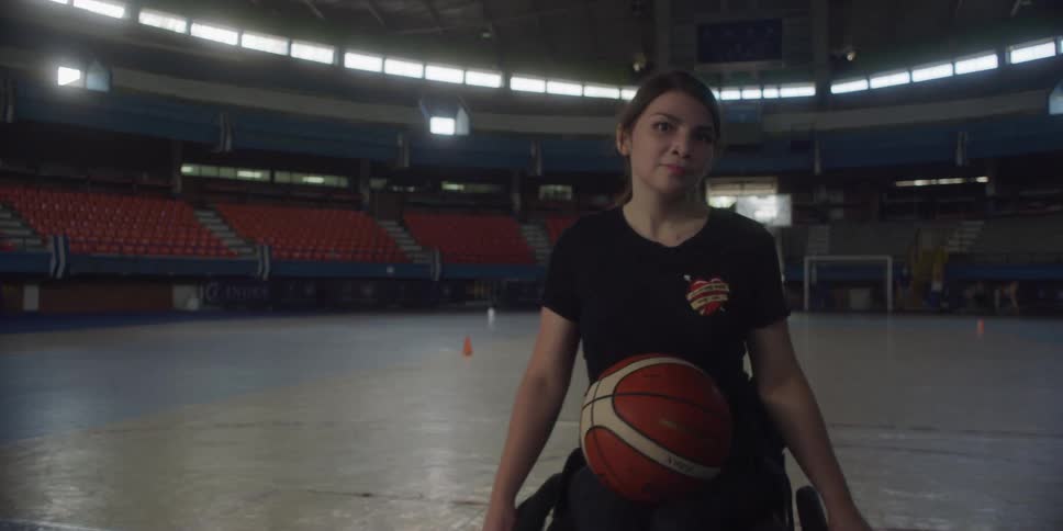 A girl moves in her wheelchair with a basketball on the court