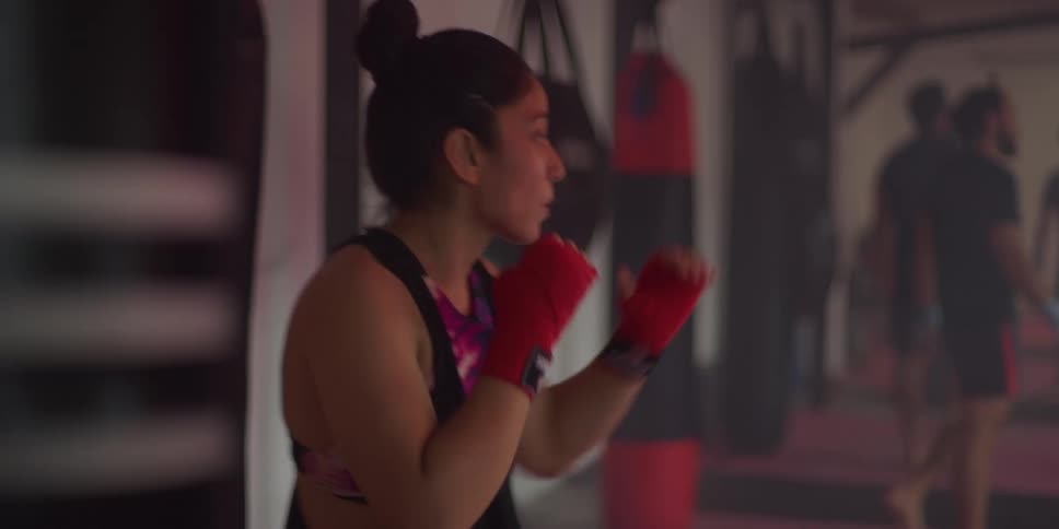 A woman kicks and punches while practicing in the gym