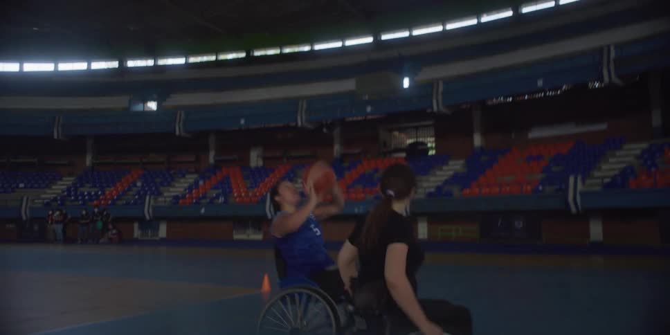 Two women in wheelchairs practicing basketball with one successfully shooting a ball into a hoop