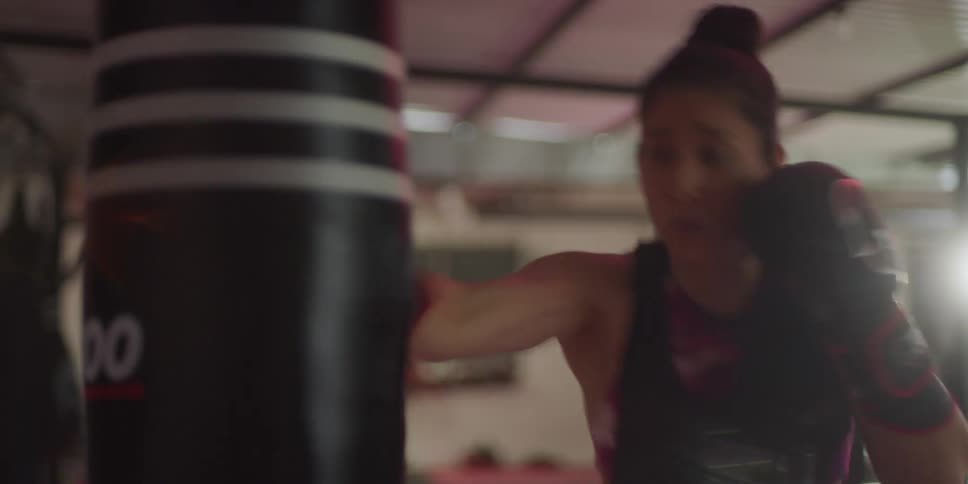 A woman is punching the heavy bag in the gym