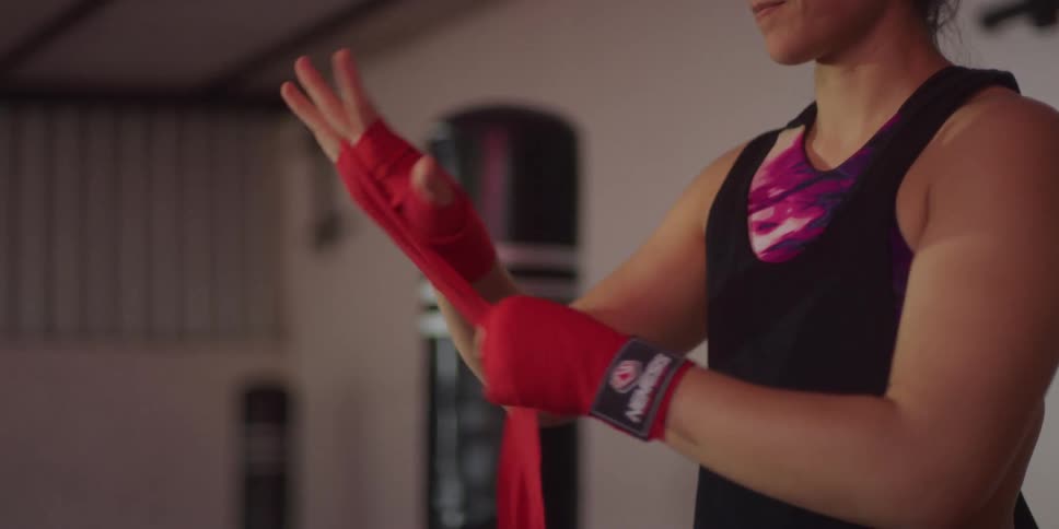 A young woman is wrapping her arm with a red cloth as she prepares for boxing training inside the gym