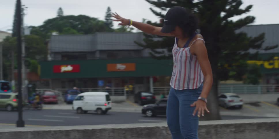Woman in cap riding skateboard in a square and balancing her body