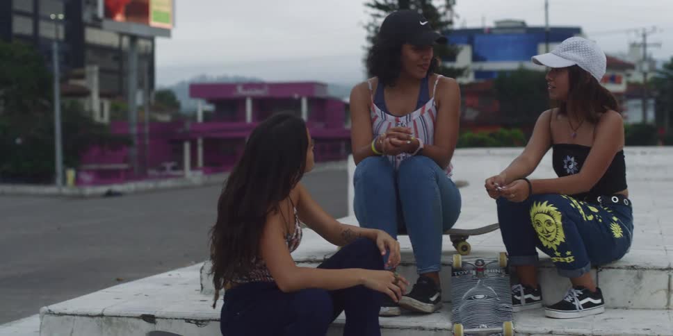 Young women sitting in a square chatting happily and with a skateboard
