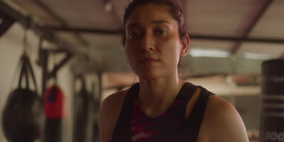 A woman with her hair pulled back wraps her hands with red boxing wraps her expression focused and serious