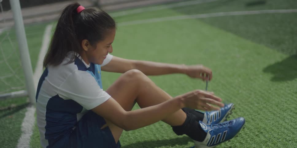 Woman sitting on a corner of synthetic grass and tying her boots