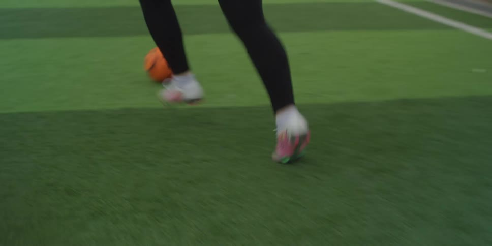 A person kicks a soccer ball on a green field as players run past their legs and feet in motion