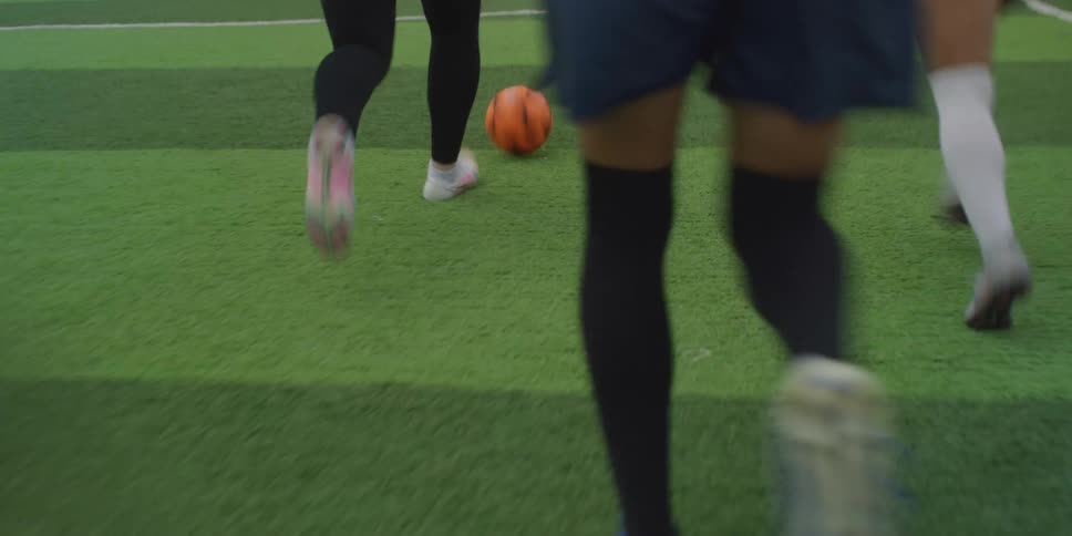A group of women playing a soccer game with one dribbling the ball around before kicking it towards the goal post hitting the crossbar