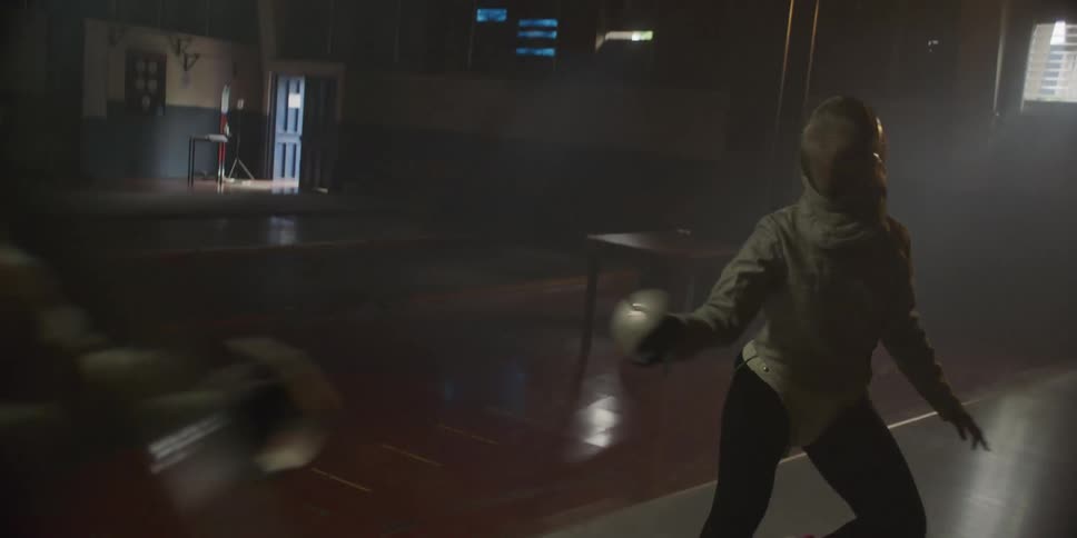 A woman puts on a fencing helmet and fences with another person on a court