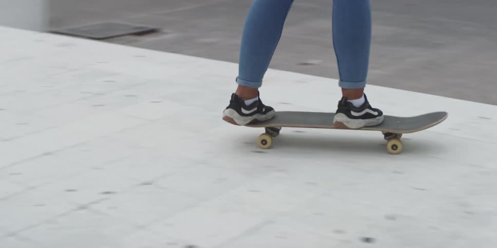 A person wearing jeans and black and white sneakers rides a skateboard on a paved surface