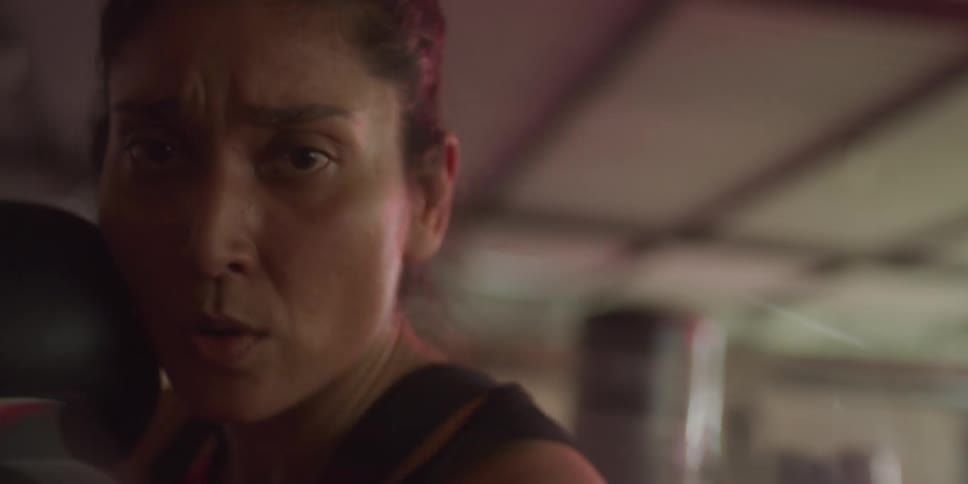 A woman wearing boxing gloves is shadowboxing vigorously in a gym as part of her boxing training