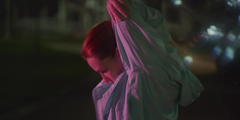 A woman is stretching on the side of the road at night wearing a jacket