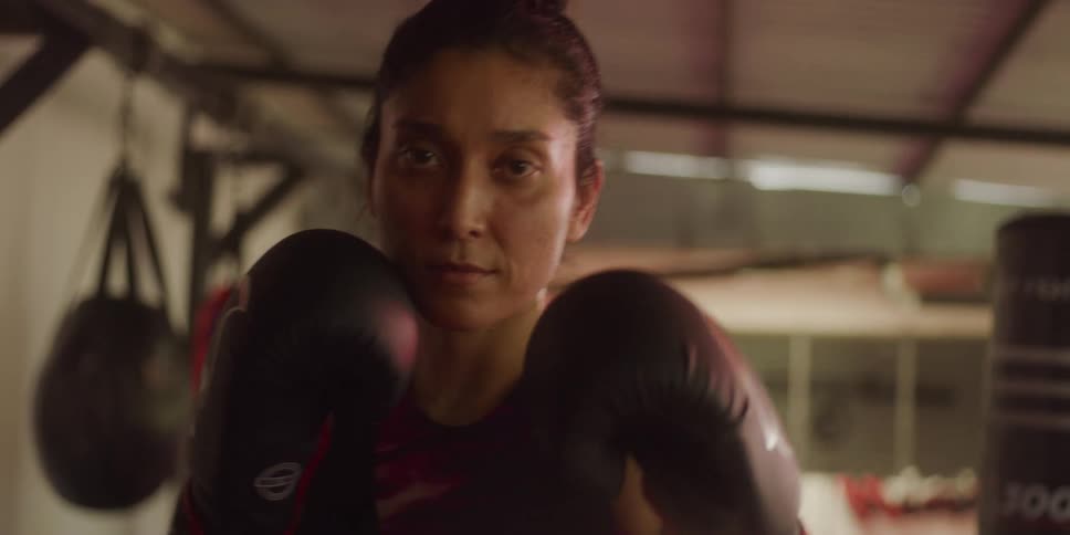 A young woman wearing gloves is practicing boxing in the gym
