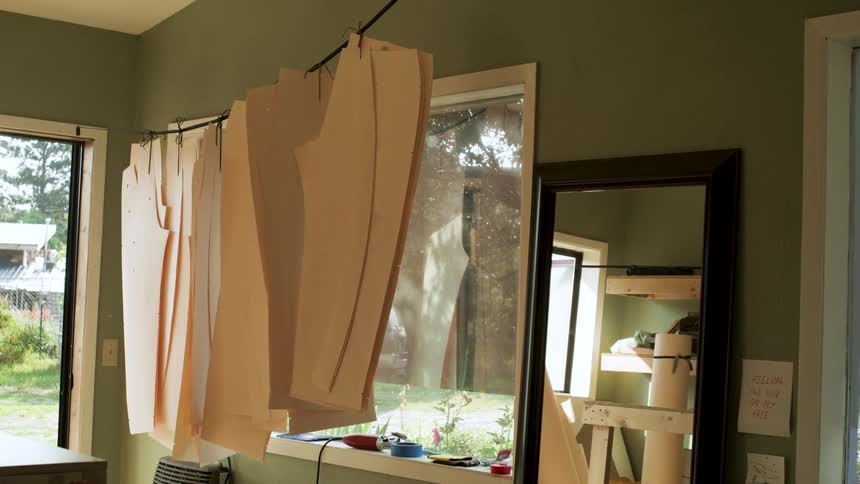 Patterns hang from a wire in a greenwalled room with a mirror and assorted items on the windowsill