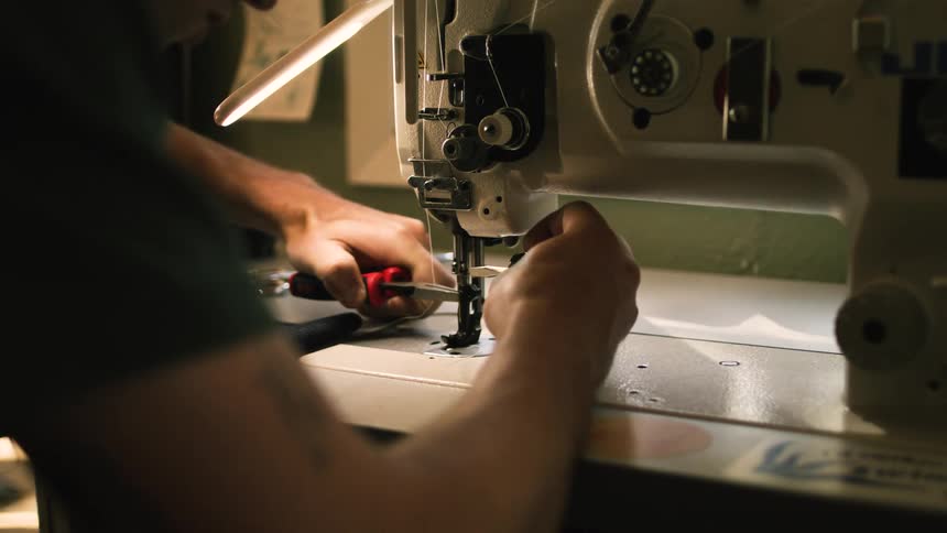 Pair of hands with tools adjusting a sewing machine