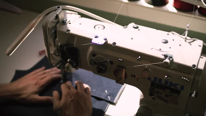 Pair of hands of a man working on a fabric on a sewing machine