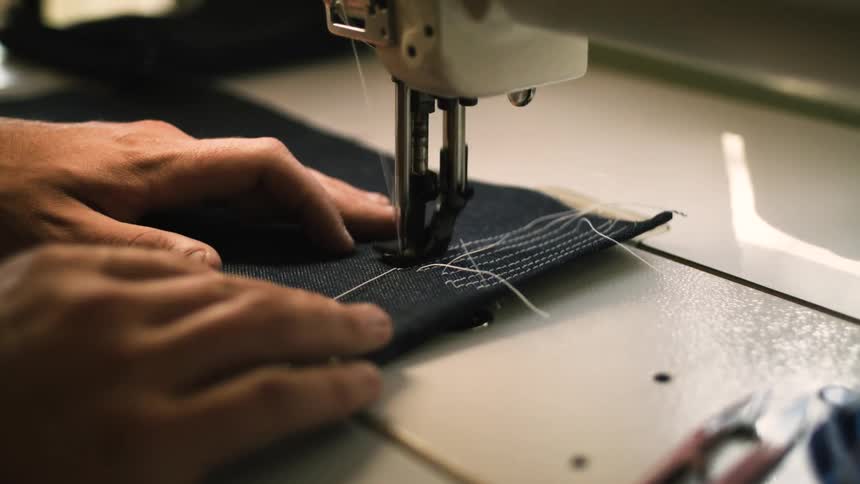 A person operates a sewing machine carefully guiding fabric with their hands