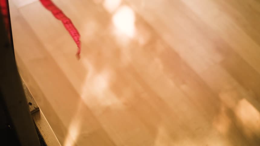 A soft measuring tape is hanging from a higher surface and dangling in the wind at midday with sunlight reflecting on the wooden floor