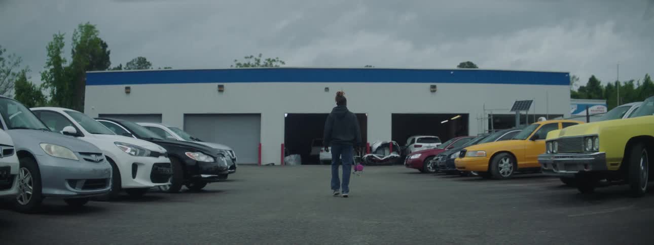 A man walks toward and enters a garage with several cars parked outside