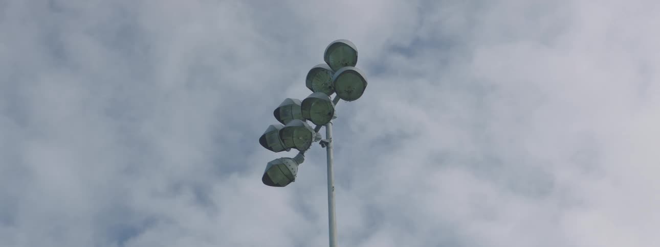 A tall metal pole contains a large group of stadium lights on a cloudy day