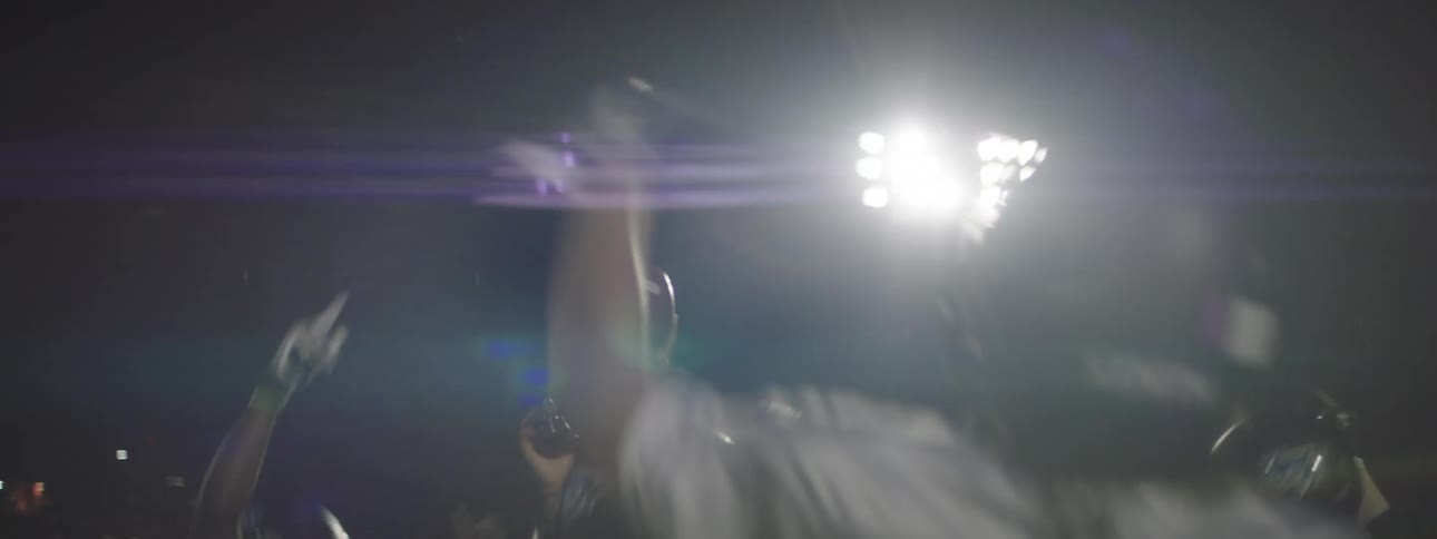 Men in football uniforms are jumping and celebrating as one holds up a football