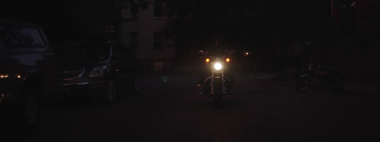A person is riding a motorcycle through a suburban neighborhood at night