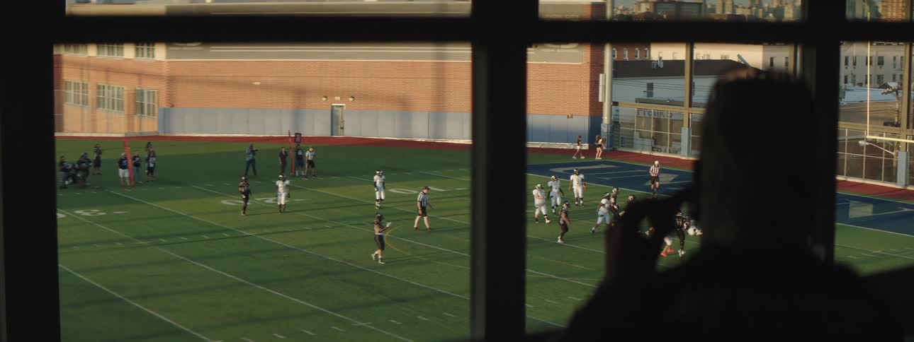 Man uses binoculars to watch two football teams during a daytime football game