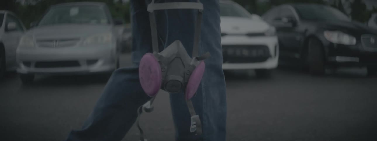 A man is holding a gas mask as he walks through a full parking lot